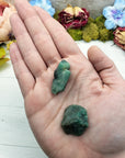 two rough emerald crystal stones in hand