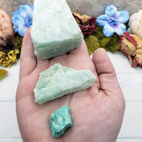 Hand holding three rough amazonite crystals, each of different sizes from large to small