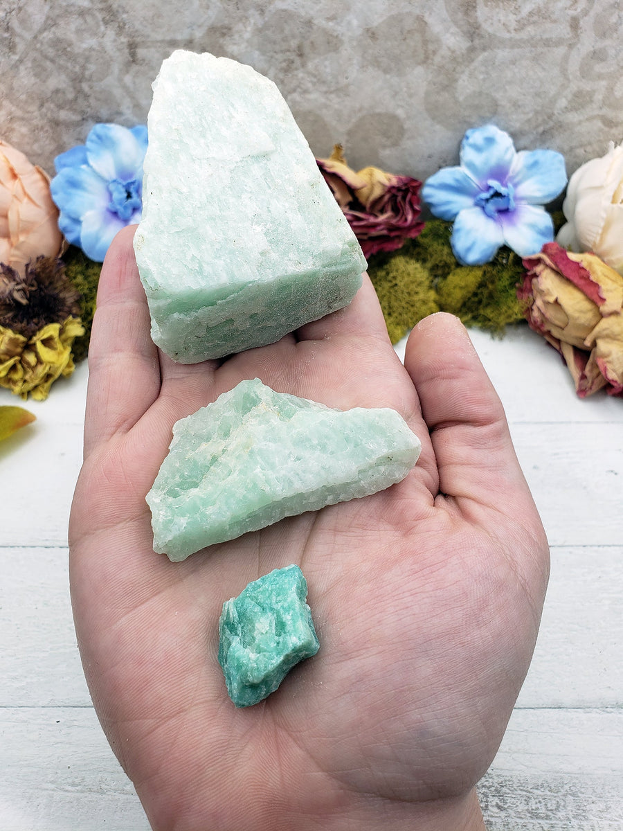 Hand holding three rough amazonite crystals, each of different sizes from large to small