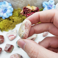 Hand pinching rhodocrosite crystal
