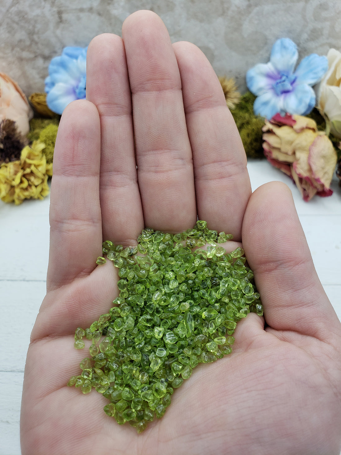 Hand holding one ounce of peridot stone chips