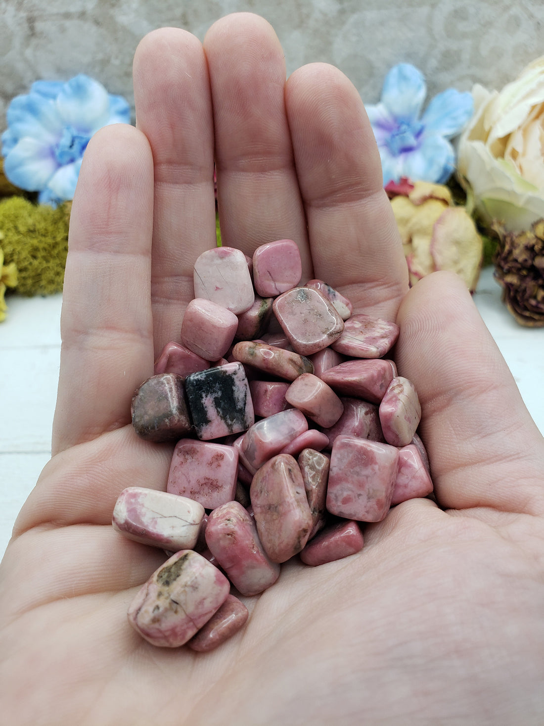 Hand holding three ounces of rhodonite pebbles