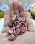 Hand holding three ounces of rhodonite pebbles