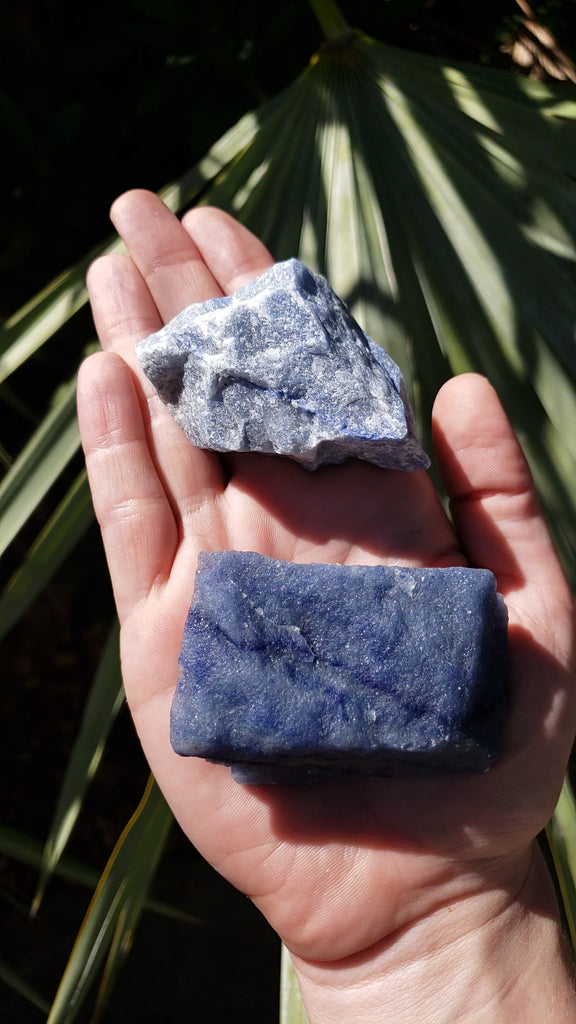 Video of hand holding two rough blue quartz crystal pieces in sunlight