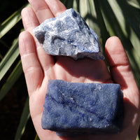 Video of hand holding two rough blue quartz crystal pieces in sunlight