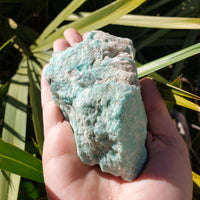 Hand holding rough amazonite stone in sunlight 