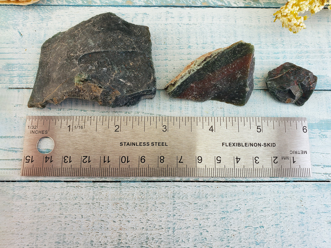 Ruler comparing size between three rough bloodstone crystal pieces, from large to small