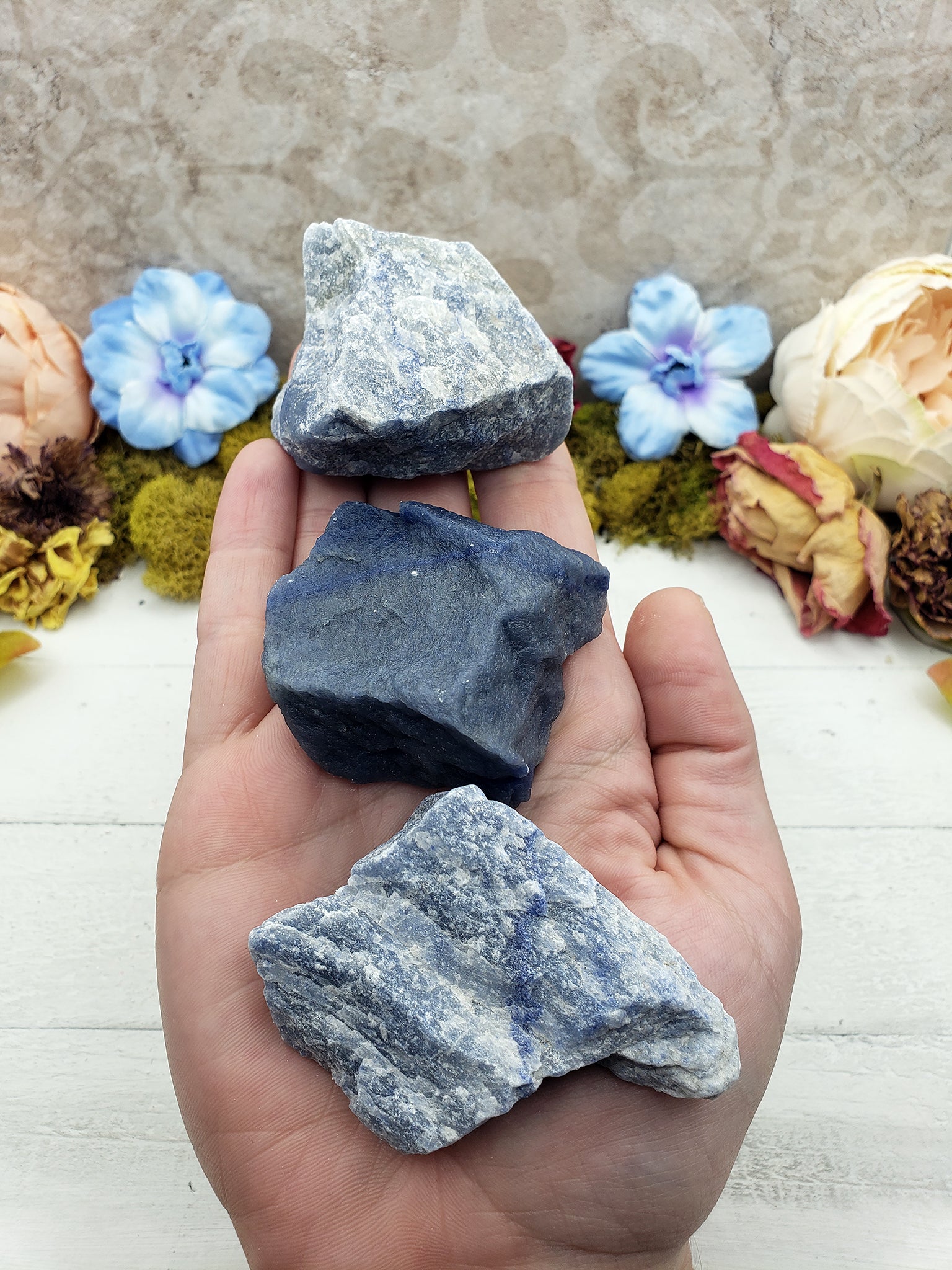 hand holding three rough blue quartz stone chunks