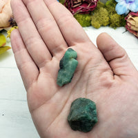 two rough emerald crystal stones in hand