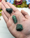 hand holding three rough emerald stone pieces