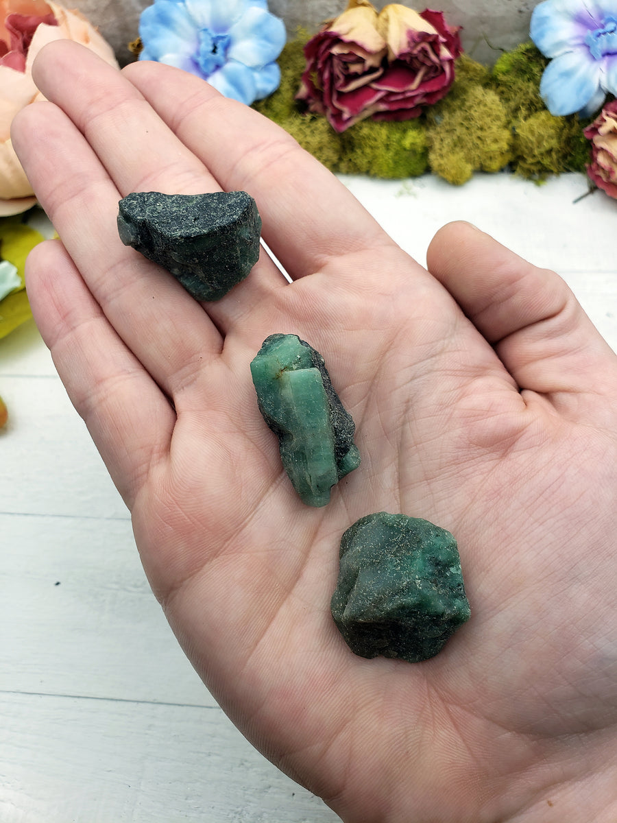 hand holding three rough emerald stone pieces