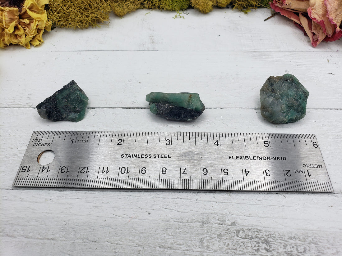 three rough emerald stone pieces on ruler comparing sizes