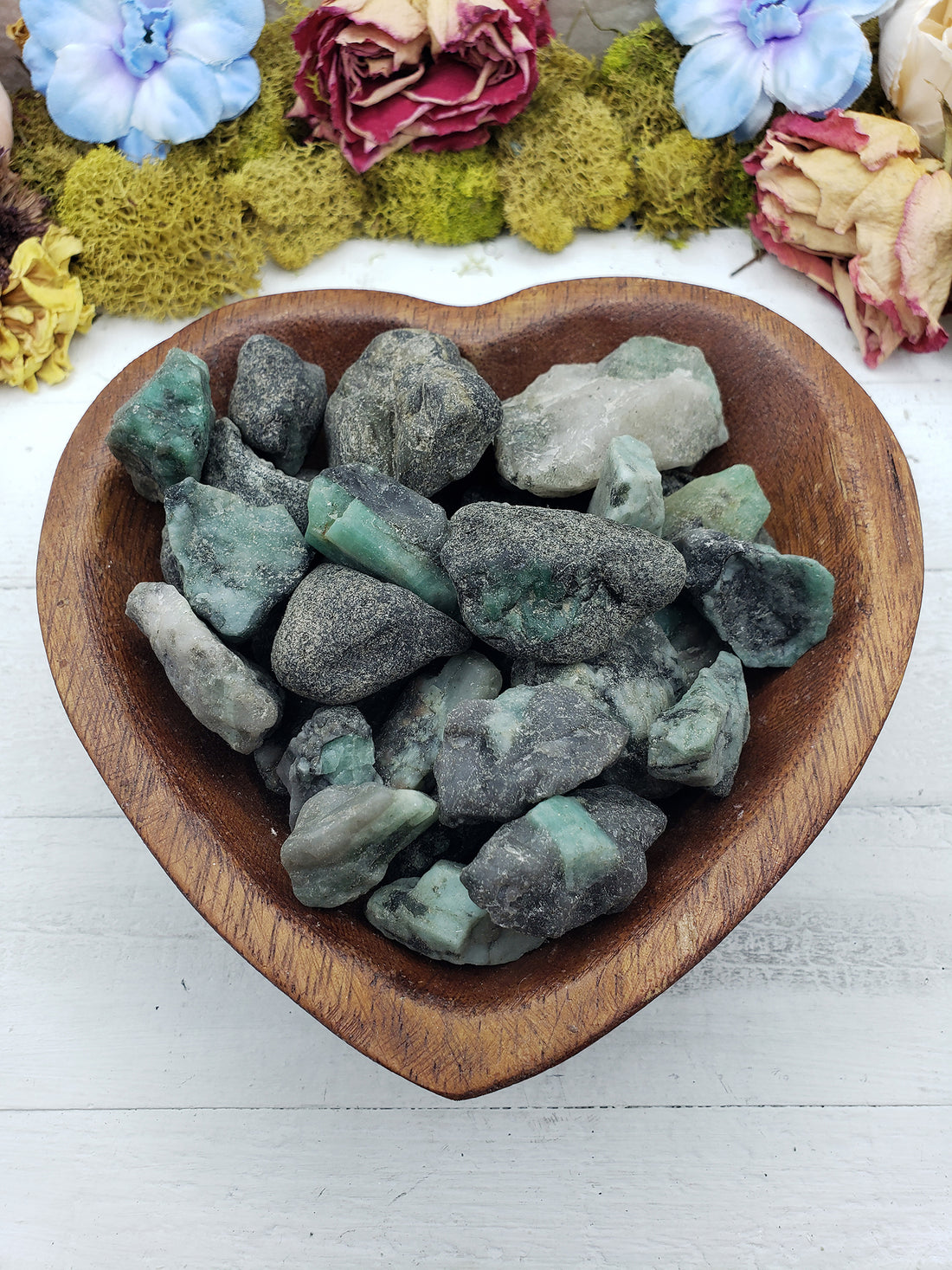 rough emerald stones in wooden heart bowl
