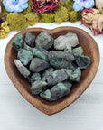 rough emerald stones in wooden heart bowl