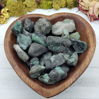 rough emerald stones in wooden heart bowl